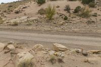 a dirt road with some rocks on the side and hills behind it is an area filled with rocks