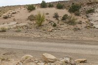 a dirt road with some rocks on the side and hills behind it is an area filled with rocks