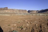 a dry area with dirt, some grass and some rocks in the foreground and the mountains