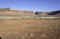 a dry area with dirt, some grass and some rocks in the foreground and the mountains