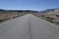 there is a empty empty road between two mountains in the distance, with a car on the side