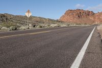 an empty highway running through the desert, with a hill in the distance and a sign on the side of the road