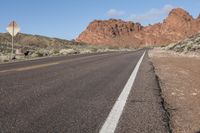 an empty highway running through the desert, with a hill in the distance and a sign on the side of the road