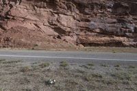 a person riding a motorcycle along a narrow road through rocks and sand cliffs a grassy area on both sides