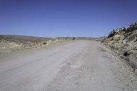 a gravel road leads to an open field of tall rocks, in a mountainous setting