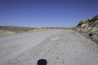 a gravel road leads to an open field of tall rocks, in a mountainous setting