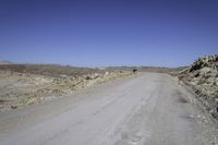 a gravel road leads to an open field of tall rocks, in a mountainous setting