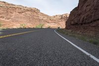 a person riding a motorcycle along a narrow road through rocks and sand cliffs a grassy area on both sides