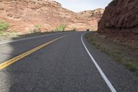 a person riding a motorcycle along a narrow road through rocks and sand cliffs a grassy area on both sides