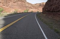 a person riding a motorcycle along a narrow road through rocks and sand cliffs a grassy area on both sides