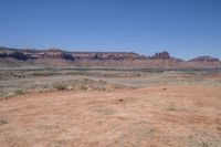 a dirt road through a desert plain with a mountain behind it and a clear blue sky in the background