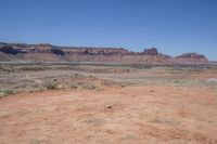 a dirt road through a desert plain with a mountain behind it and a clear blue sky in the background