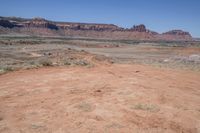 a dirt road through a desert plain with a mountain behind it and a clear blue sky in the background