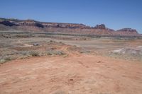 a dirt road through a desert plain with a mountain behind it and a clear blue sky in the background