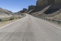 an empty highway is passing along the mountainside of a desert area, surrounded by dry grass and rocks