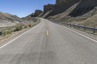 an empty highway is passing along the mountainside of a desert area, surrounded by dry grass and rocks