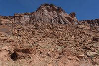 the top of a rocky hill covered in lots of brown rocks and sparse grass near a blue sky