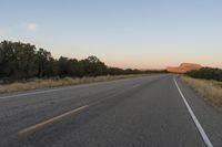 a long empty road with mountains in the distance with a car in the foreground