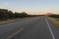 a long empty road with mountains in the distance with a car in the foreground