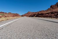 a desert road with small vegetation along both sides of it and a thin strip of white lines running along the road