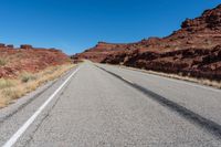 a desert road with small vegetation along both sides of it and a thin strip of white lines running along the road