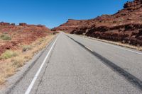 a desert road with small vegetation along both sides of it and a thin strip of white lines running along the road