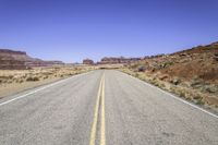 the desert and the highway are long and empty with yellow lines on them, with blue skies behind it