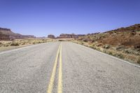 the desert and the highway are long and empty with yellow lines on them, with blue skies behind it