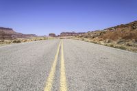 the desert and the highway are long and empty with yellow lines on them, with blue skies behind it