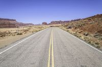 the desert and the highway are long and empty with yellow lines on them, with blue skies behind it