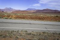 a wide open road running through a desert landscape near mountains and rocks by the side