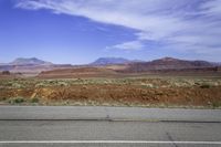 a wide open road running through a desert landscape near mountains and rocks by the side