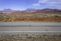 a wide open road running through a desert landscape near mountains and rocks by the side