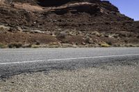 motorcycle driving along a road by a rock formation and desert mountains are in the background