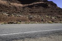 motorcycle driving along a road by a rock formation and desert mountains are in the background