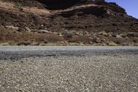 motorcycle driving along a road by a rock formation and desert mountains are in the background