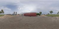 there is a red shed sitting in the middle of a large dirt lot in a rural town