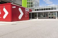 a red shipping container is at an intersection with another building and a street sign near it