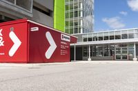 a red shipping container is at an intersection with another building and a street sign near it