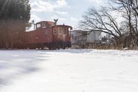 a red train car on tracks in the snow in front of houses and trees with trees