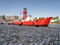 a red tug boat with a light tower in the background of a city and water