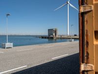 red and white lighthouse and street sign on side of road with wind turbines in background