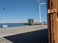 red and white lighthouse and street sign on side of road with wind turbines in background