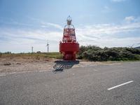 red and white lighthouse and street sign on side of road with wind turbines in background