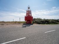 red and white lighthouse and street sign on side of road with wind turbines in background