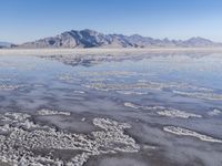 the ocean and mountains are reflected in the shallow water of the desert beach, near the horizon