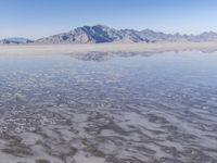 the ocean and mountains are reflected in the shallow water of the desert beach, near the horizon