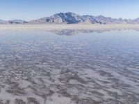 the ocean and mountains are reflected in the shallow water of the desert beach, near the horizon