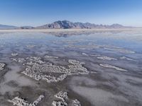 the ocean and mountains are reflected in the shallow water of the desert beach, near the horizon