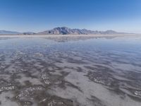 the ocean and mountains are reflected in the shallow water of the desert beach, near the horizon